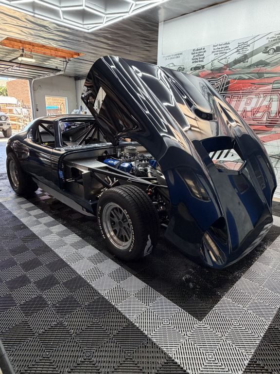 Black sports car with gullwing doors open on a patterned floor in a modern showroom