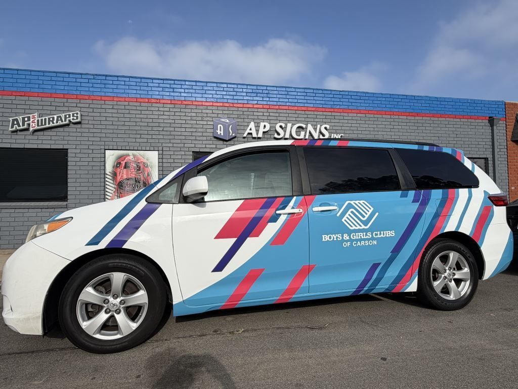 Wrapped white hatchback with blue and pink stripes parked outside an A1 Signs shop