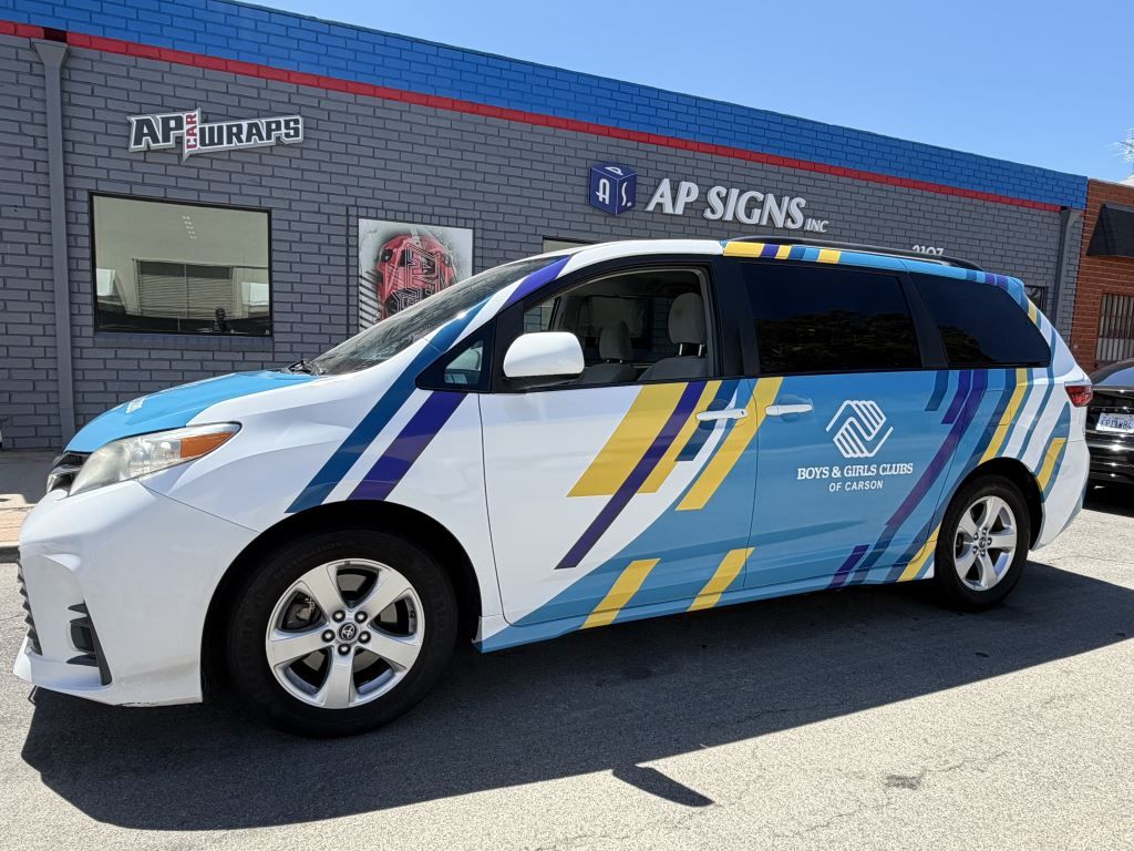 Wrapped white minivan with blue and gold graphics parked outside the AP Signs building