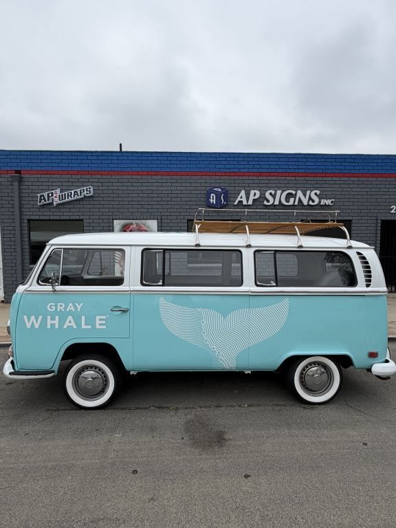 Light blue and white vintage van with whale mural parked outside an AP Signs building.