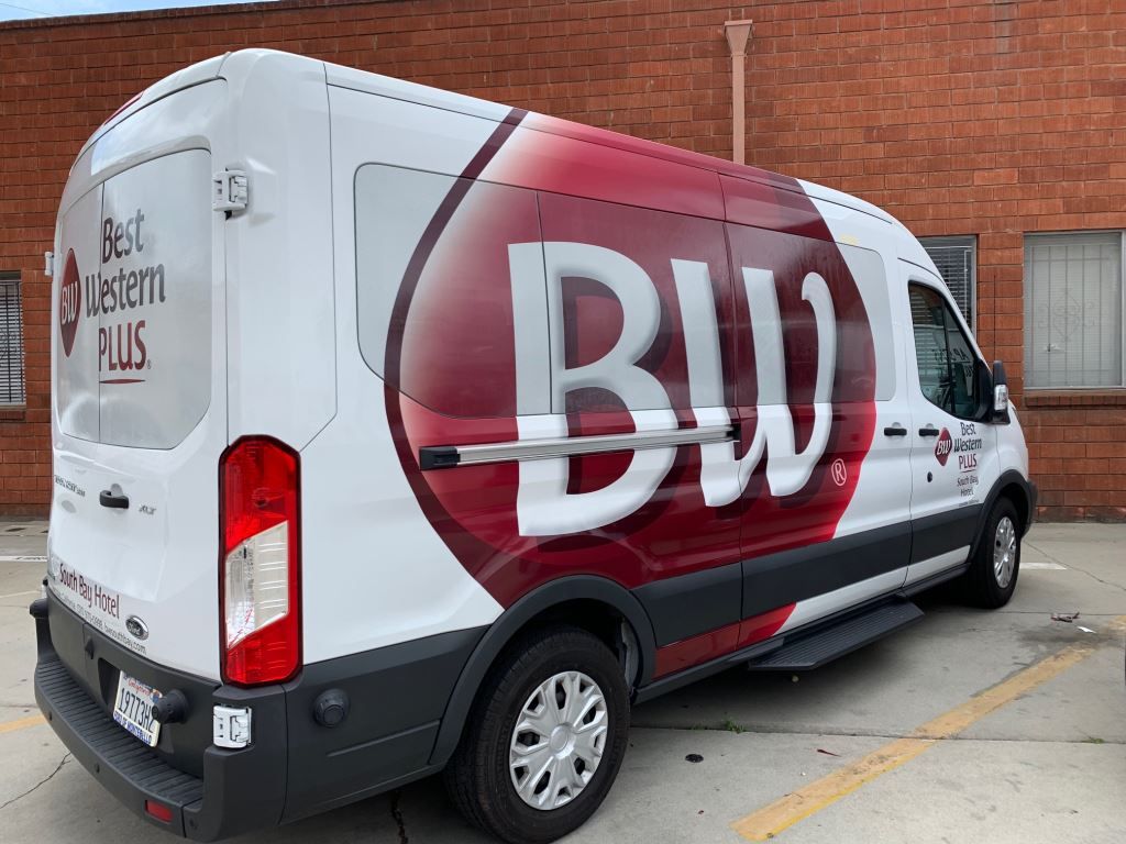White BWI delivery van with a large maroon logo parked beside a brick building