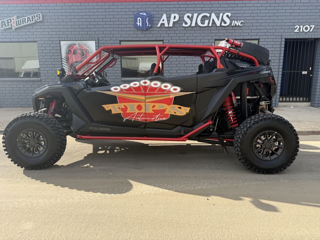 Black off-road UTV with red roll cage and graphics parked outside AP Signs shop