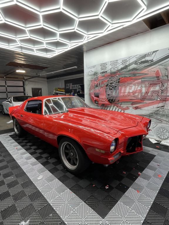Red classic muscle car in a modern showroom with hexagonal ceiling lights and mural wall artwork