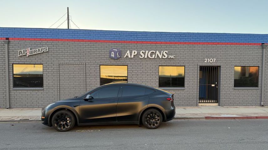 Black sedan parked in front of an AP Signs storefront on a city street