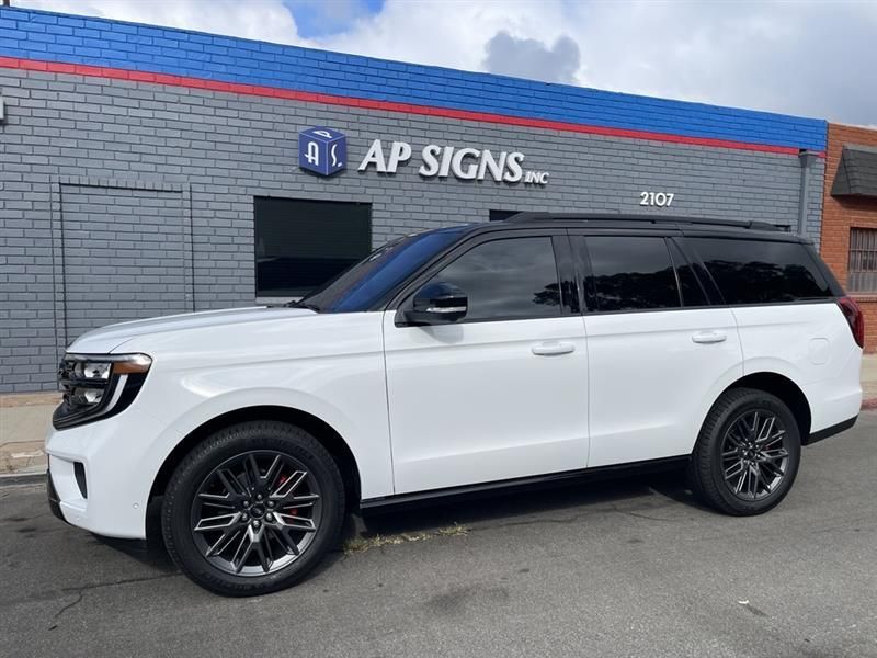 White SUV parked in front of an AP Signs storefront with gray brick wall and blue trim.
