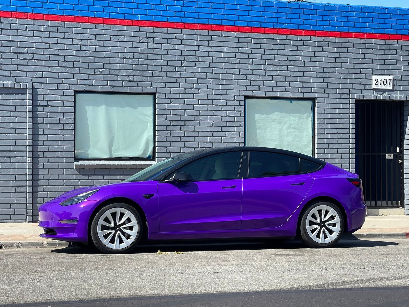 Purple sedan parked beside a gray brick building with two windows and a black door