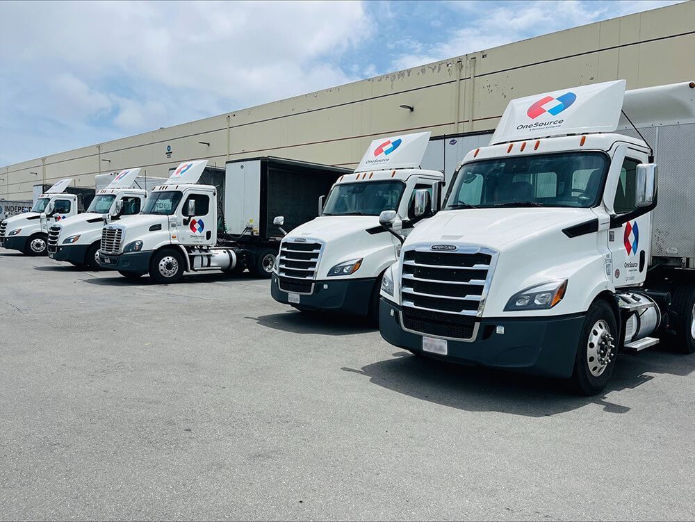 White delivery trucks lined up outside a warehouse loading dock under a clear sky.