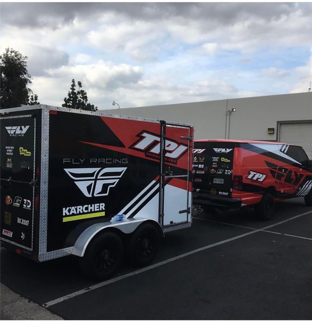 Red and white race trailers are parked in a lot, with a black trailer in the foreground.
