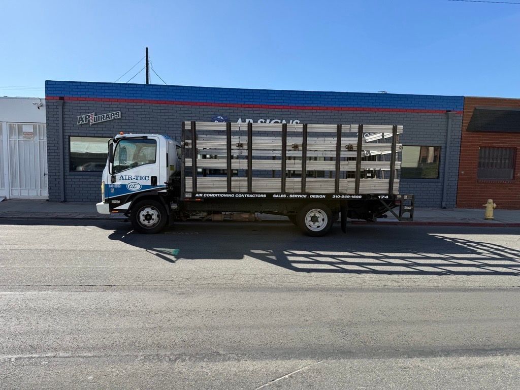White flatbed truck parked in front of a storefront with blue and red trim