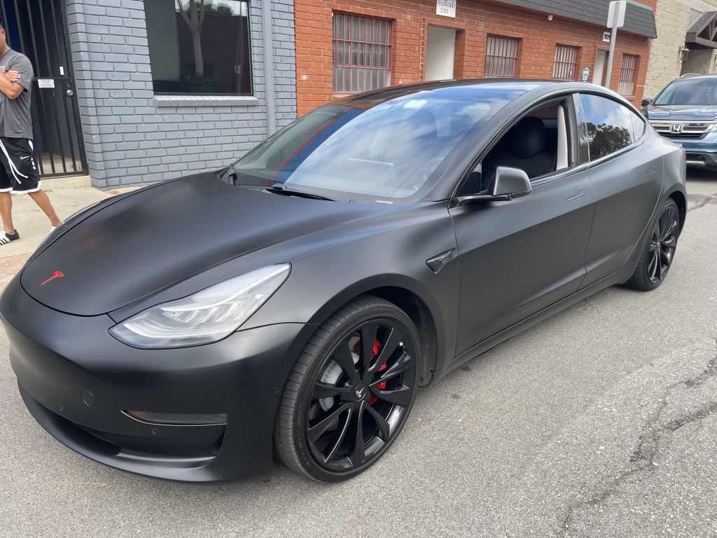 Matte black Tesla sedan parked on a street beside brick buildings