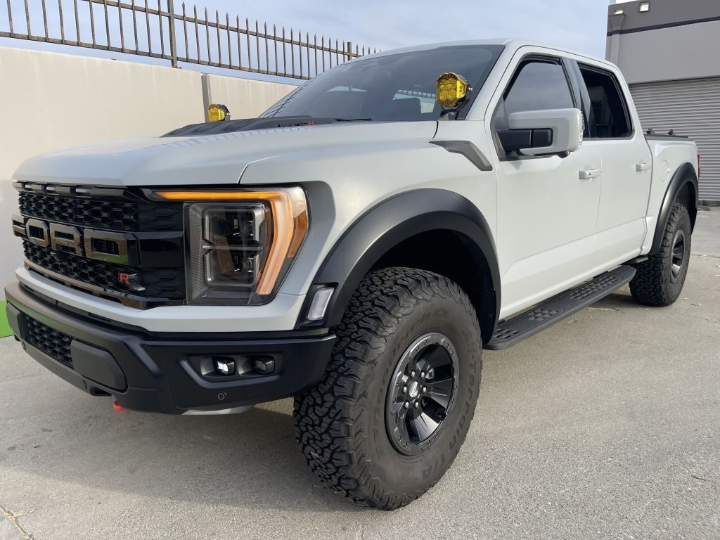 White off-road pickup truck parked outdoors by a fence, front-left view, with large tires and black trim
