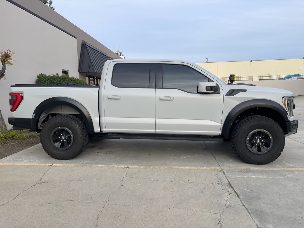 Silver pickup truck parked in a lot, side view, with black wheels and off-road tires