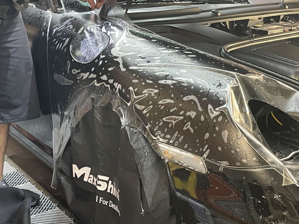 Damaged black car with shattered windshield and scraped bodywork in a workshop