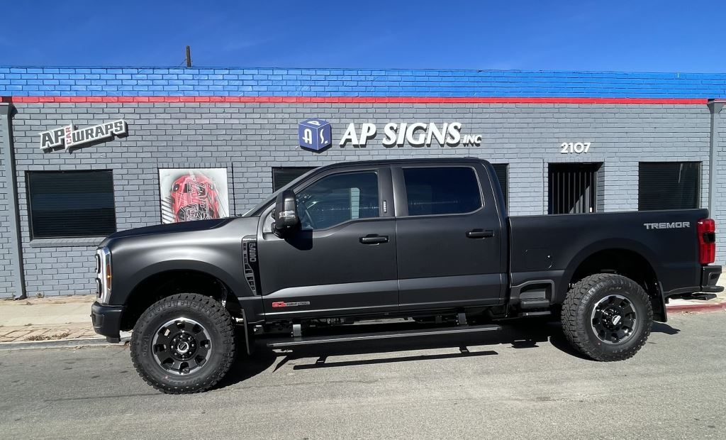 Black lifted pickup truck parked in front of AP Signs building with blue brick facade.
