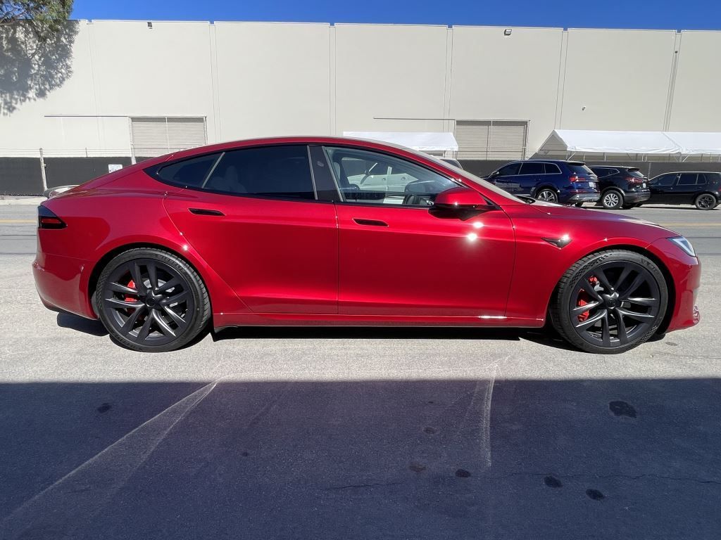 Red sedan parked in front of a beige building on a sunny day.
