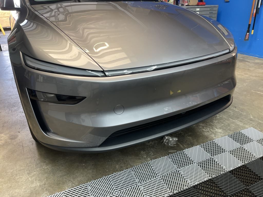 Front view of a silver Tesla sedan in a garage, with a patterned floor mat in the foreground
