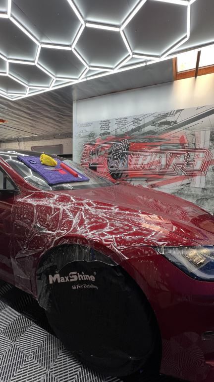 Red sports car with glass-like body art displayed indoors under geometric ceiling lights