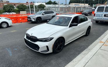 A white BMW 3 series is parked in a parking lot next to a police van.
