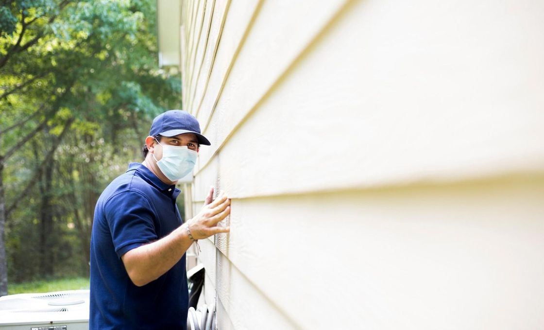 A man wearing a mask is working on the side of a house.