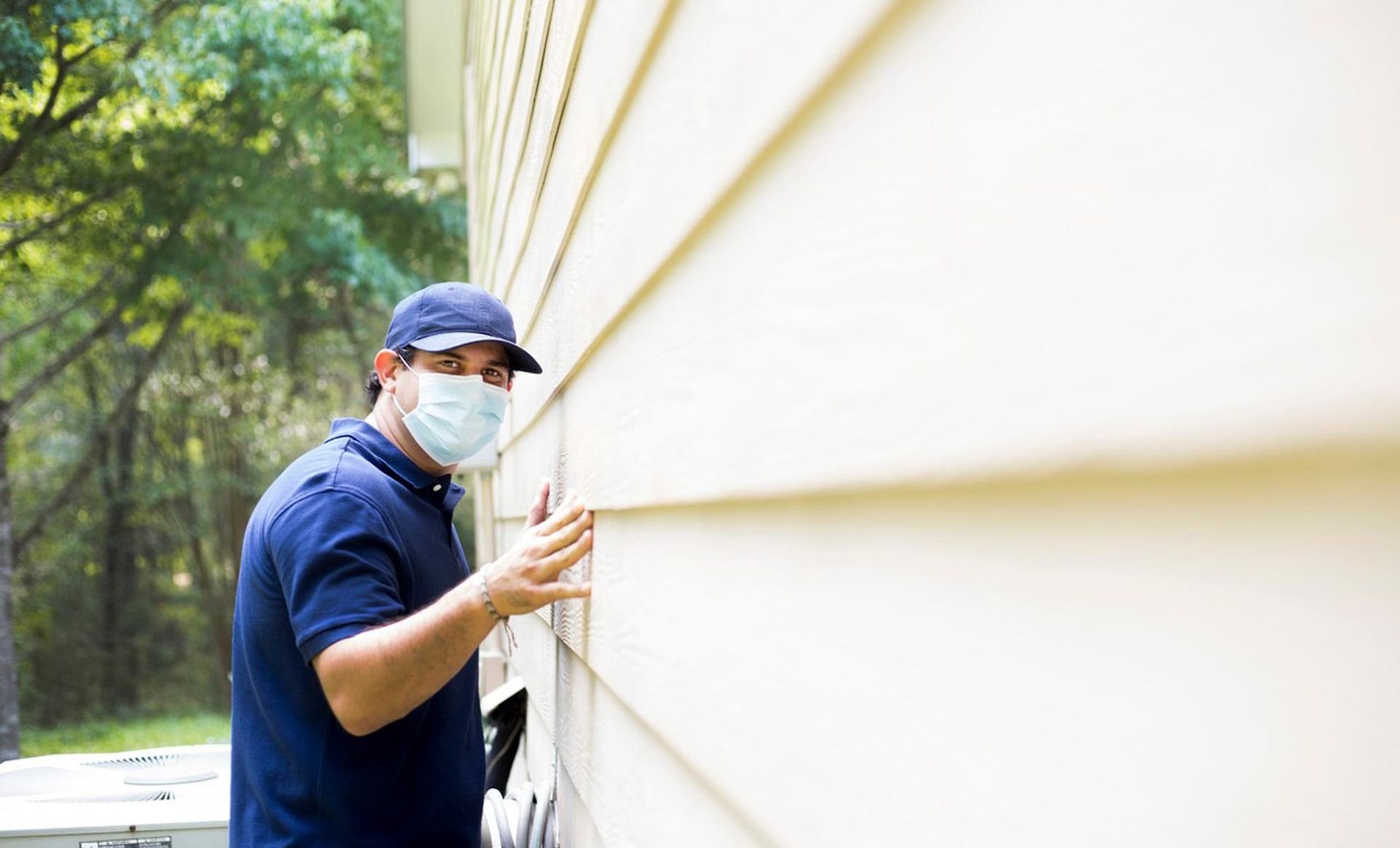 A man wearing a mask is working on the side of a house.