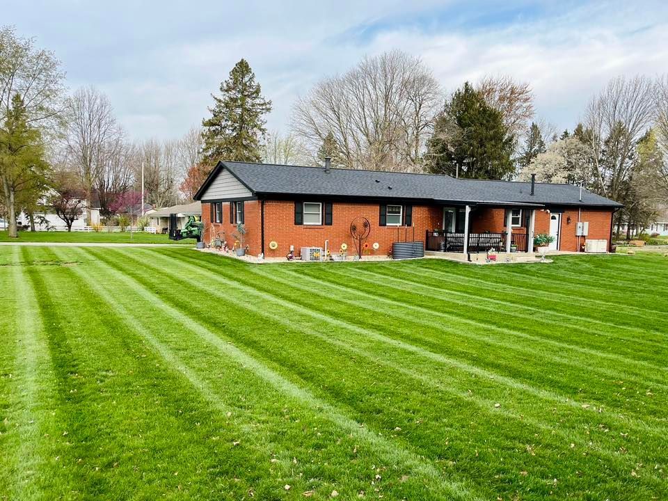 A brick house with a dark roof and porch, set on a freshly mowed lawn with striped patterns under a cloudy sky.