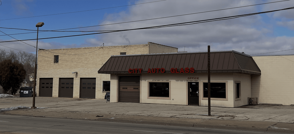 A low-rise beige commercial building with a brown roof and a street in front.