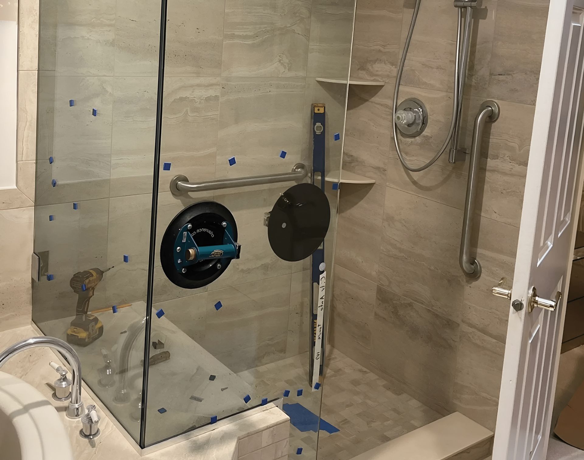 Shower with glass door being installed; level, suction cup, drill, grab bar, and shelves visible.