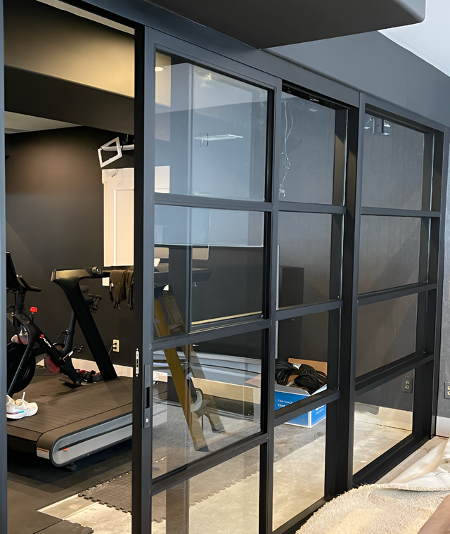 Black-framed glass sliding doors separate a gym area. A treadmill and exercise equipment are visible inside.