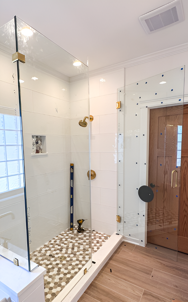 Glass-enclosed shower with gold fixtures, pebble floor, and wood-grain door. White tile walls.