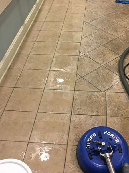 Tile floor being cleaned with a blue Hydro Force machine; floor is wet and some tiles are clean.