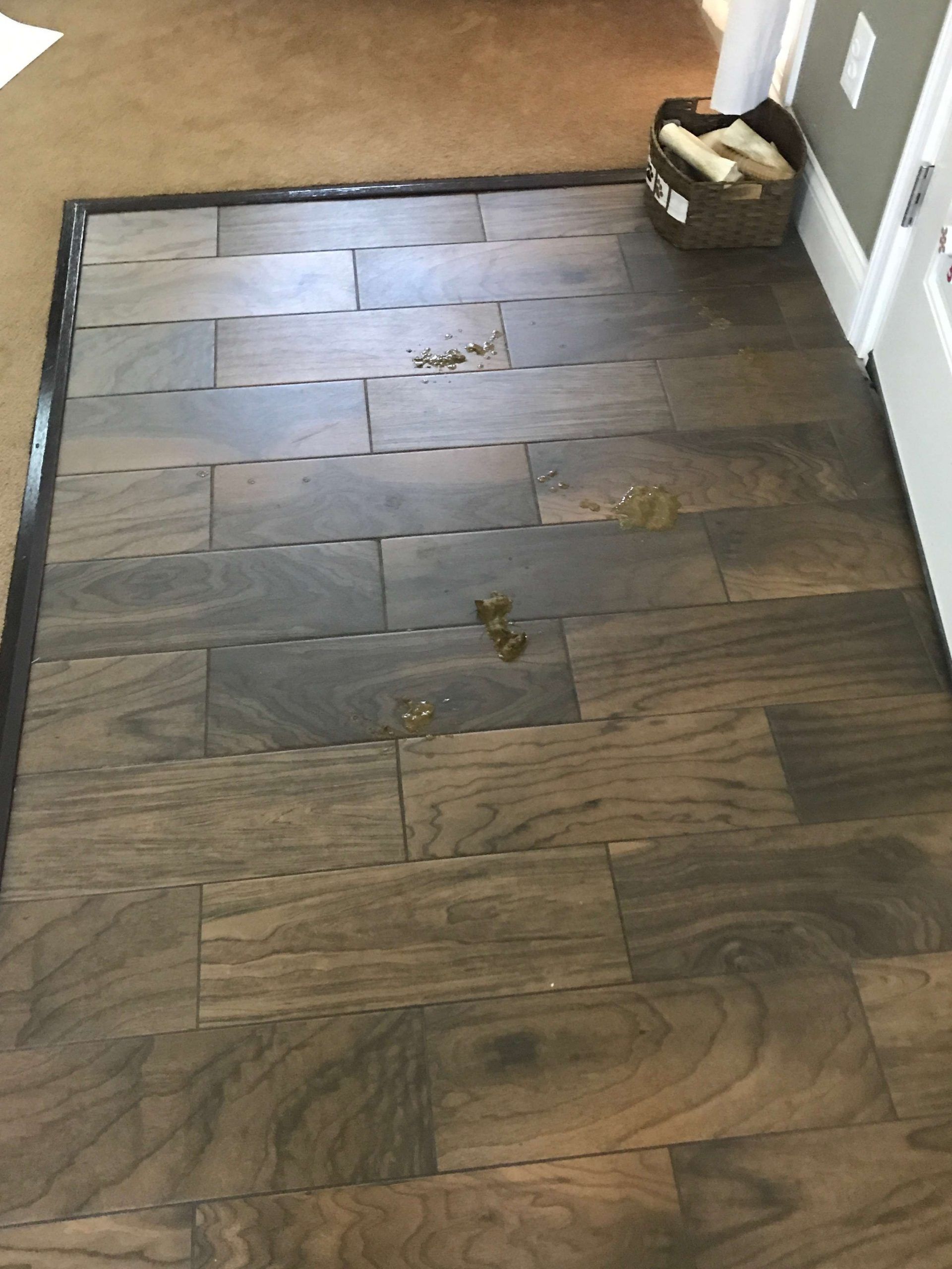 Wooden-look tile flooring in a doorway with debris scattered on it. A basket with rolled items sits in the corner.