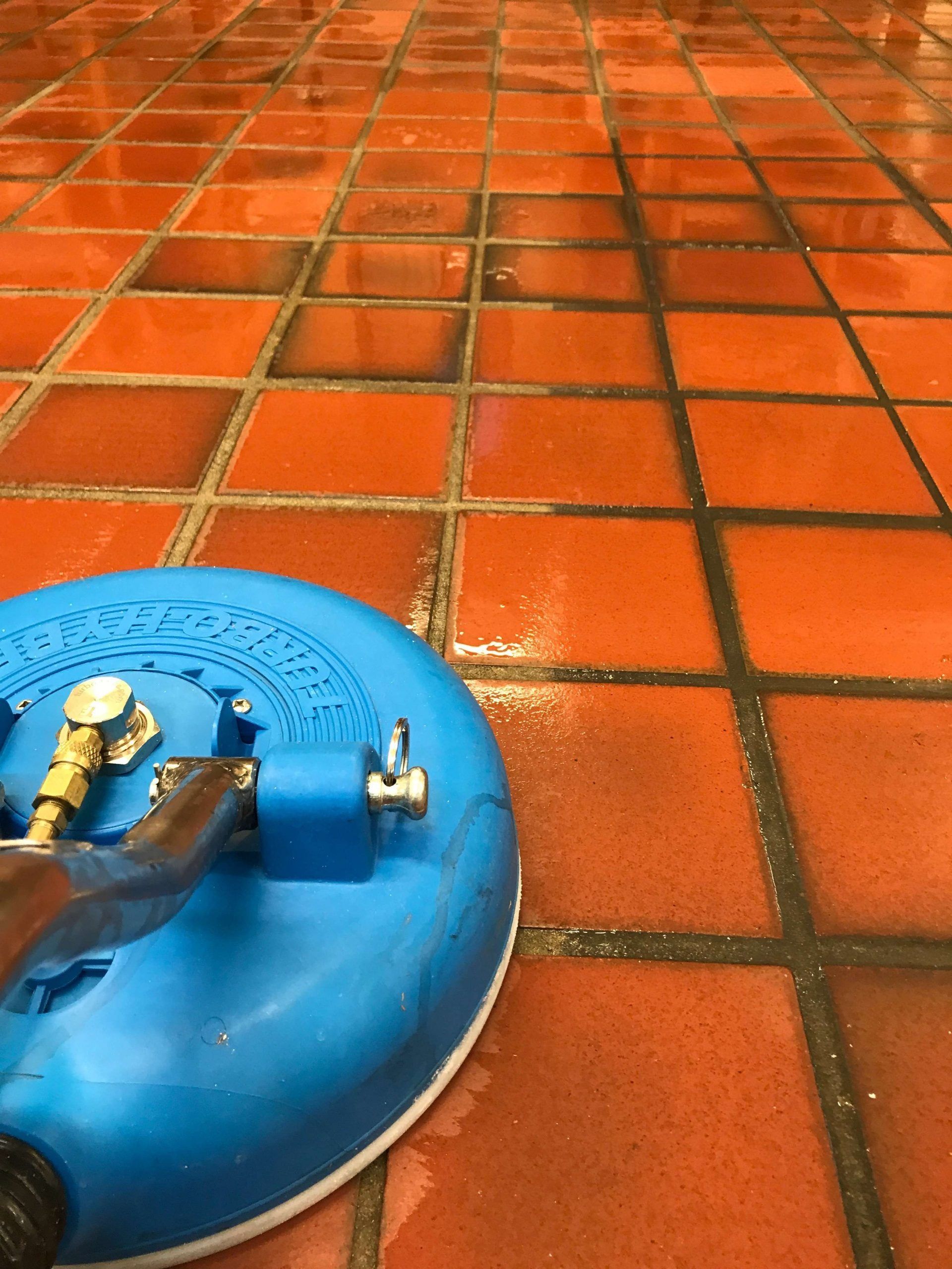 Blue power washer cleaning orange tile floor, removing dark grime.
