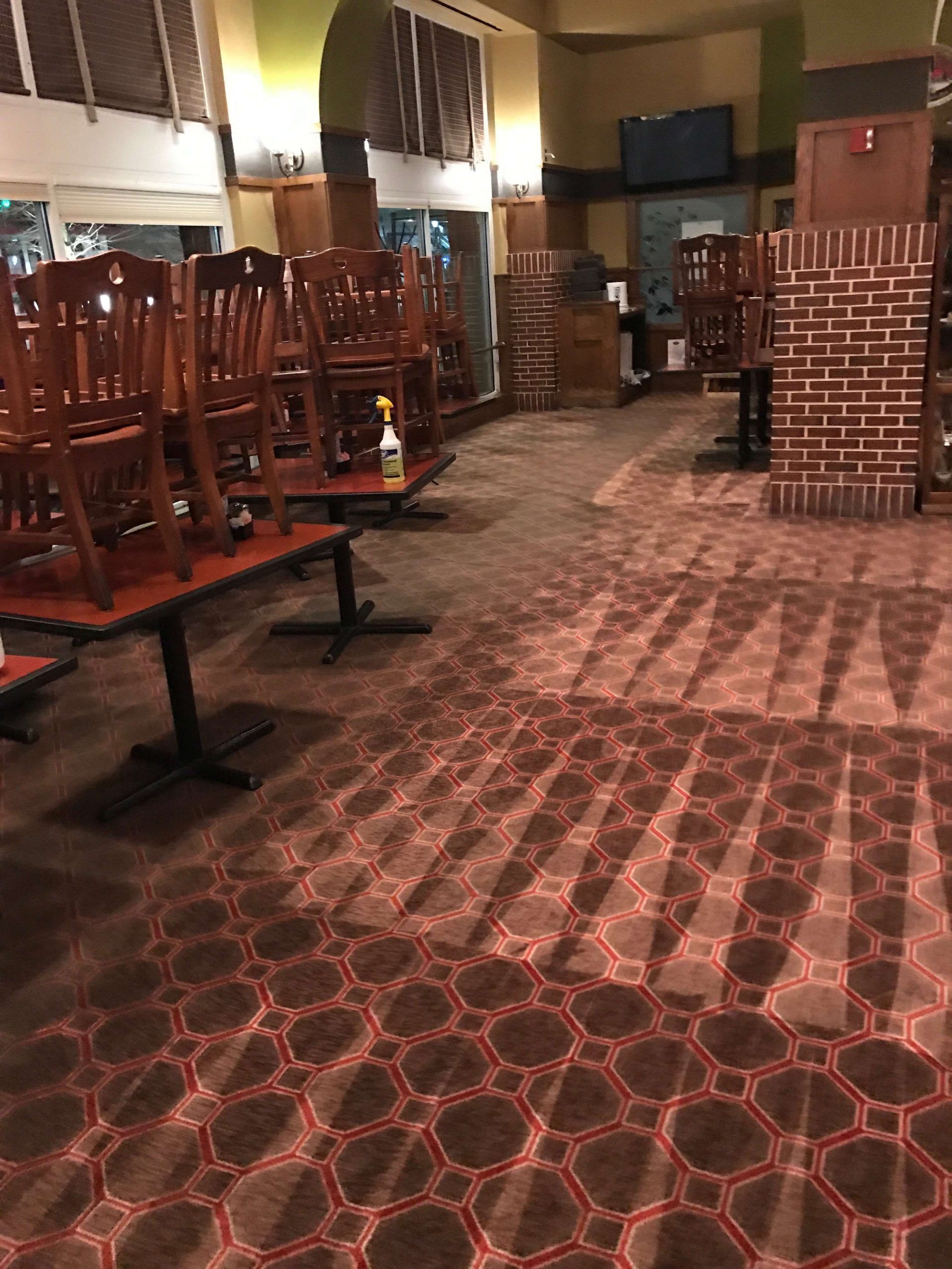 Restaurant interior with chairs stacked on tables; carpet with geometric design.