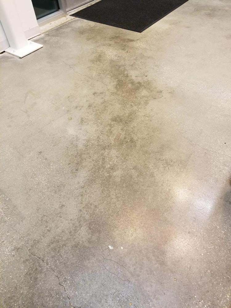 Concrete floor with dark staining near a doorway and black welcome mat.