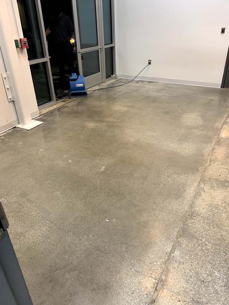 Concrete floor with visible debris near a glass door, a power outlet, and a cleaning machine.