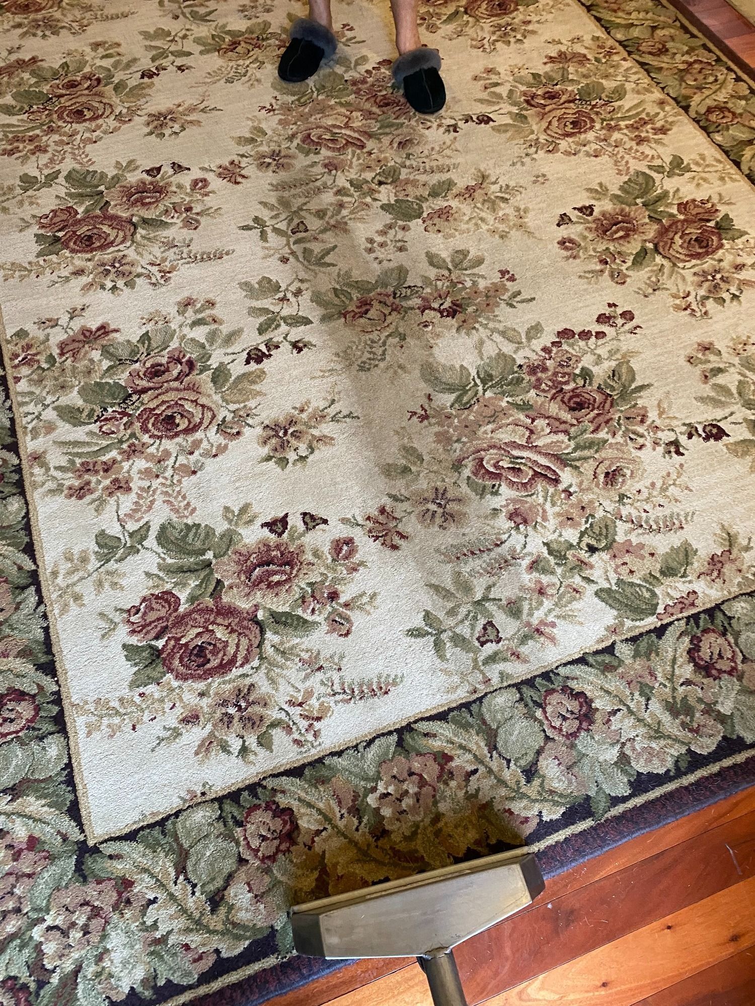 Person vacuuming floral rug with a cream and burgundy color scheme; wood floor.
