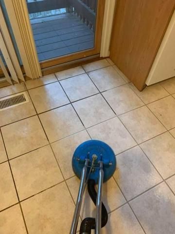 A floor cleaning machine in use on tiled floor next to a sliding glass door and wooden door.