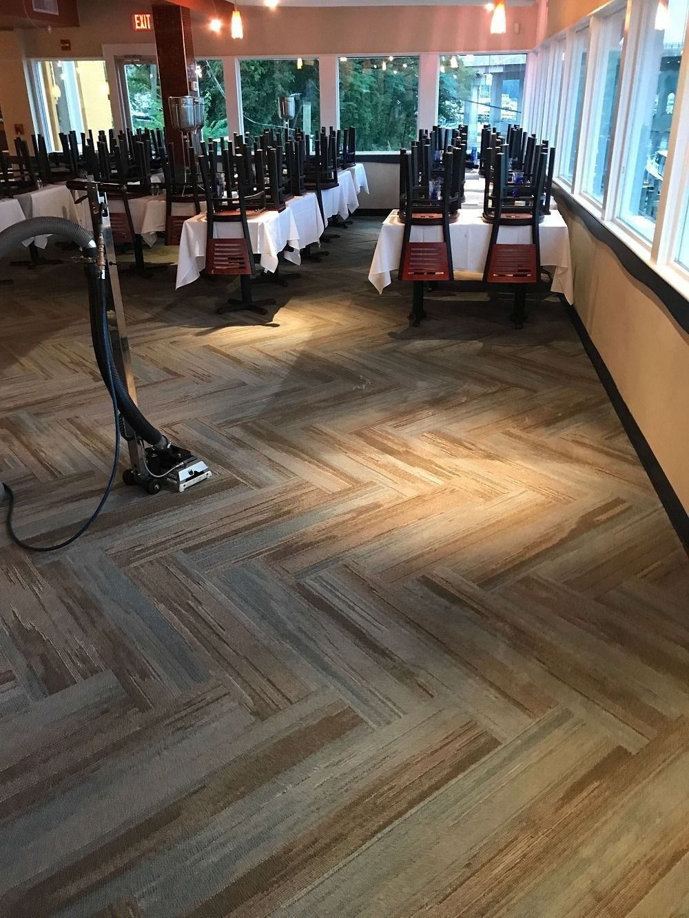 Carpeted restaurant floor with tables and chairs stacked. A vacuum cleaner is in the foreground.