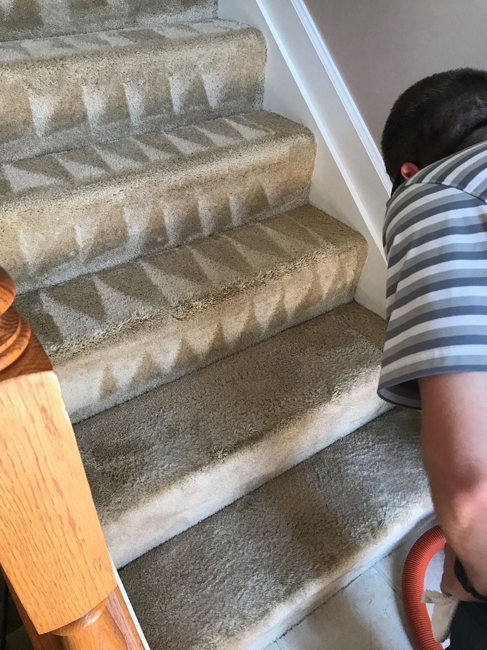 Person vacuuming carpeted stairs; beige carpet, white trim, wooden banister.