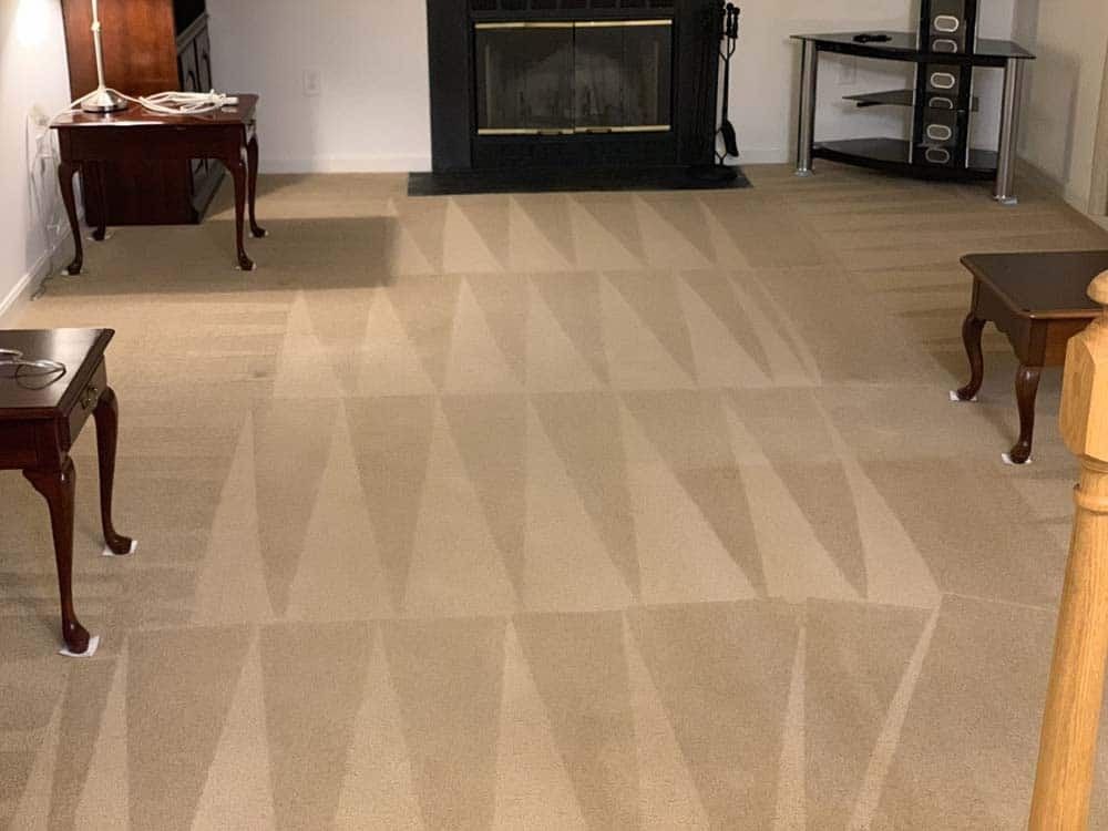 Beige carpet with geometric cleaning pattern, fireplace, and furniture in a living room.