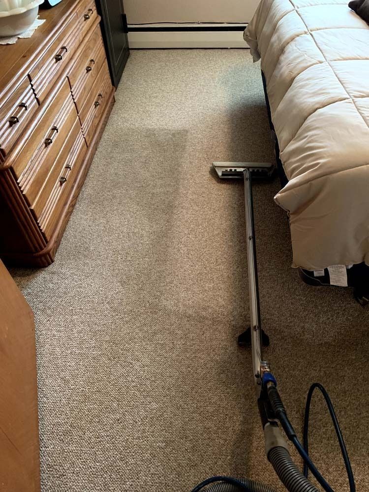 A carpet cleaner in action, removing dirt from a beige carpet in a bedroom.