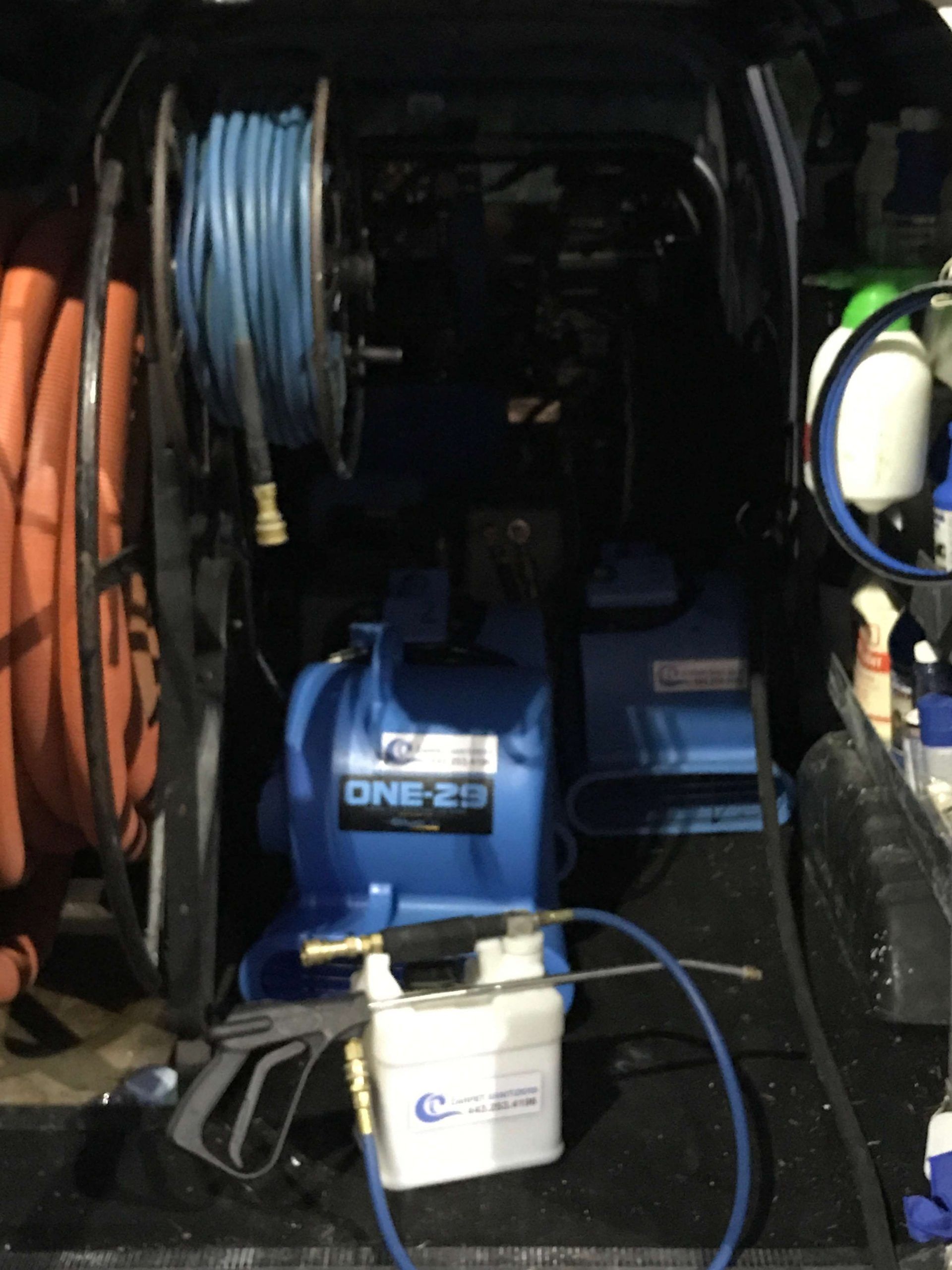 Interior of a truck with cleaning equipment: blue hose reel, water pump, spray bottles.
