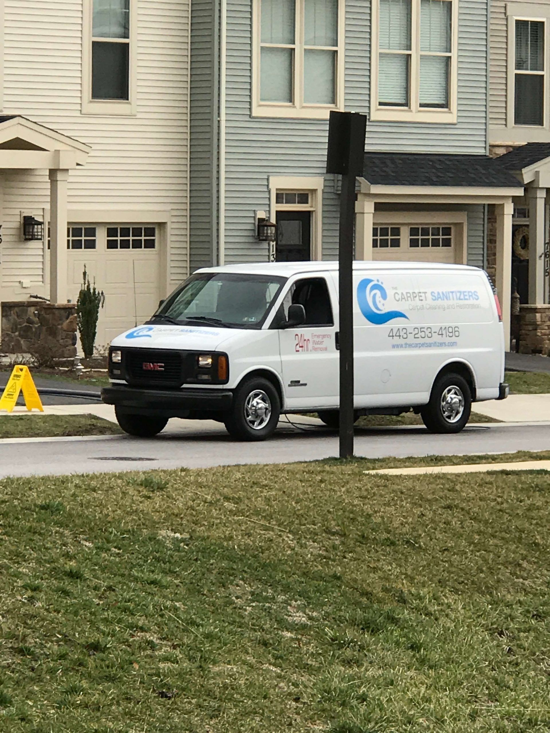 White van with company logo parked on a street in front of houses.