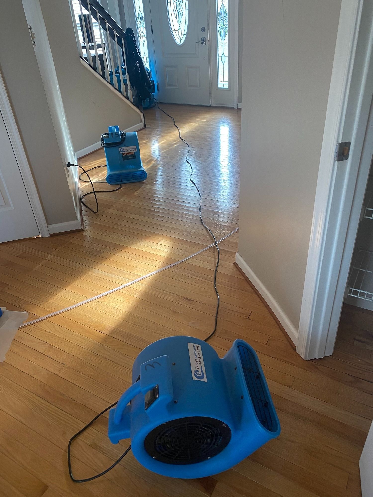 Two blue air movers on hardwood floor in a home hallway, drying water damage.