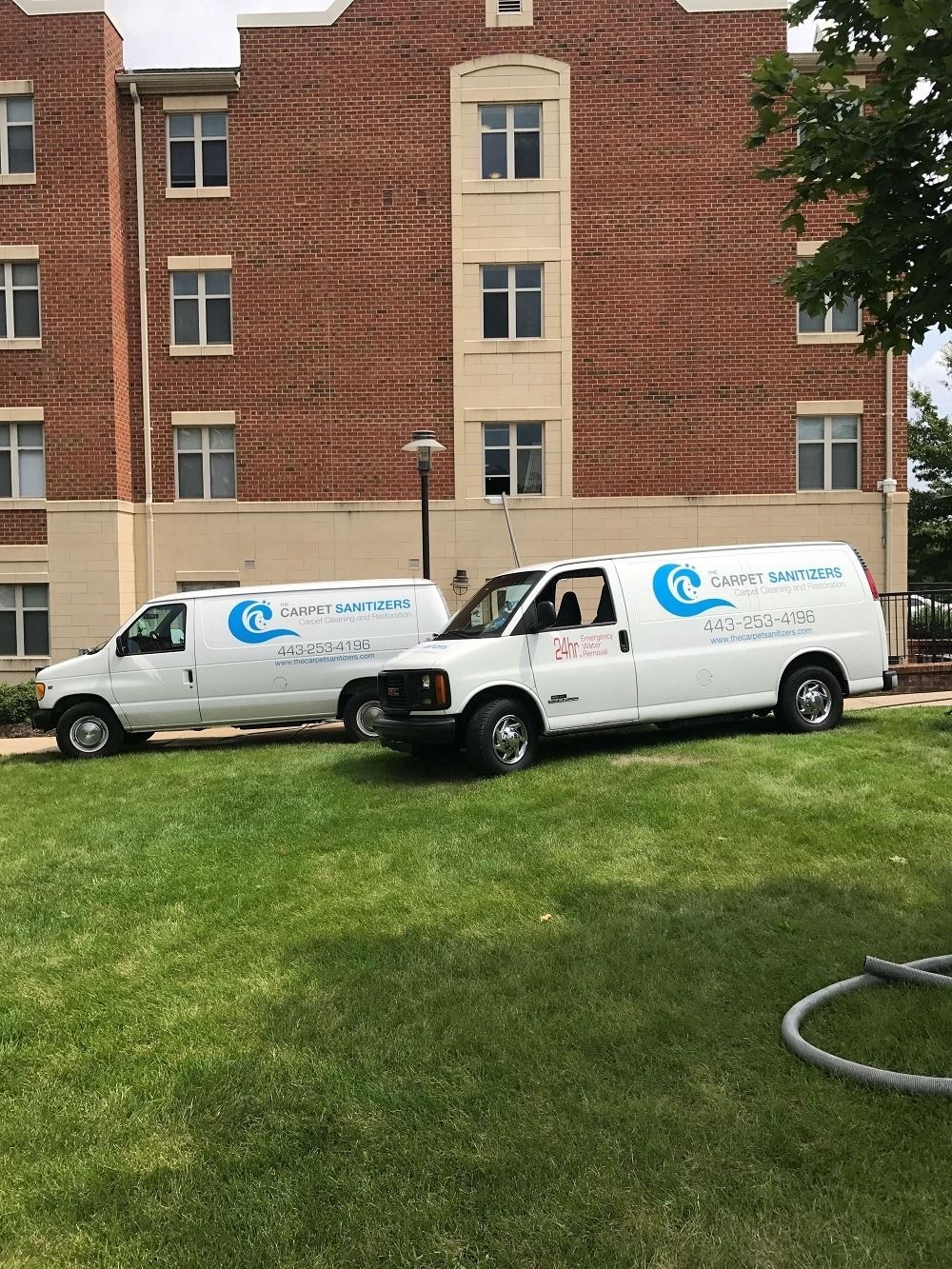 Two white service vans parked on grass in front of a brick building.
