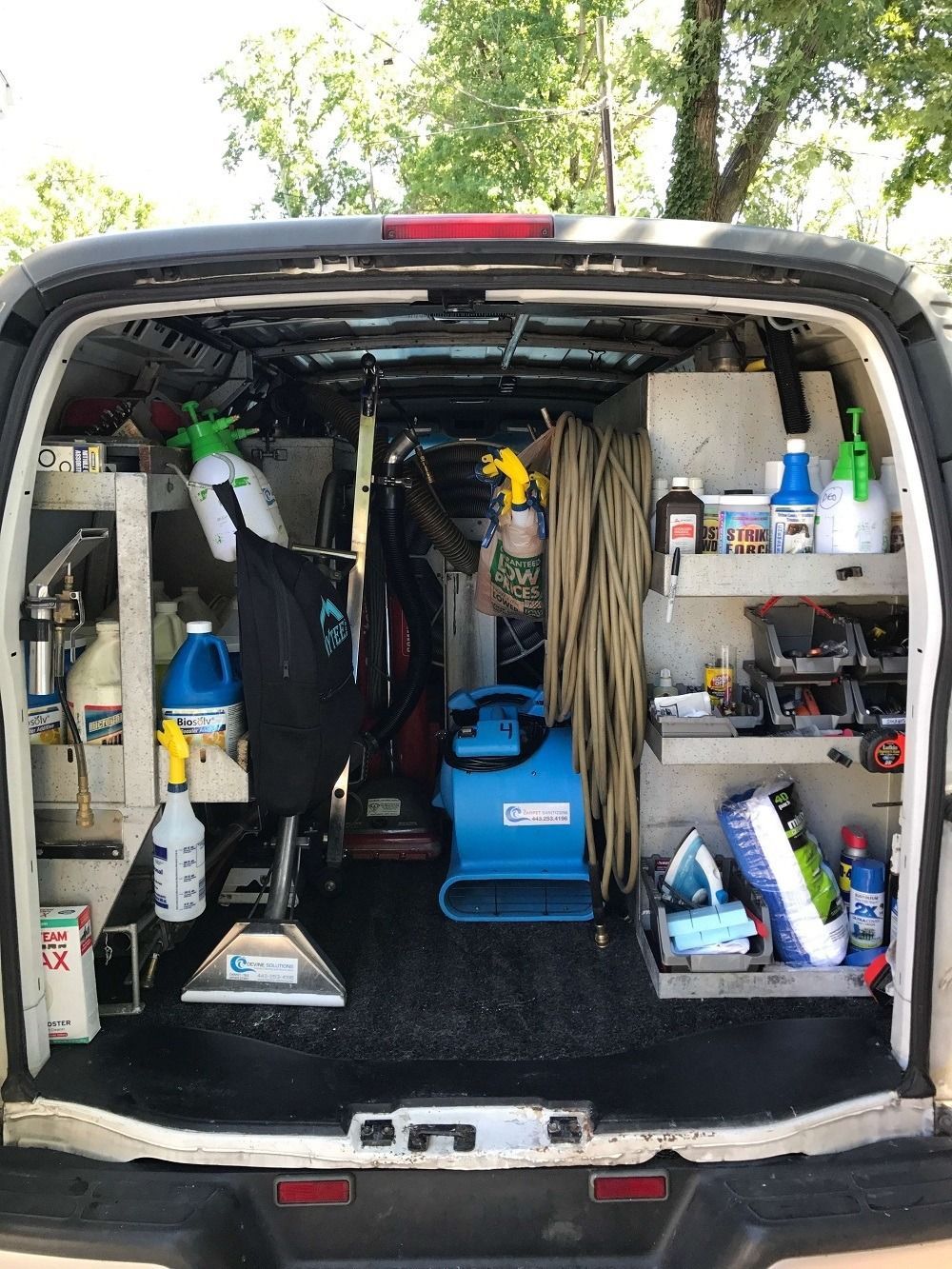Interior of a cleaning van, with equipment like carpet cleaners, spray bottles, and cleaning supplies visible.