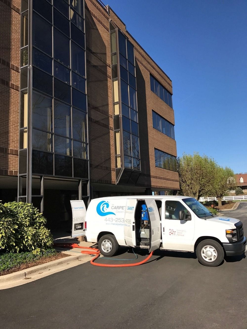 White service van with open doors and hose near a brick and glass building.