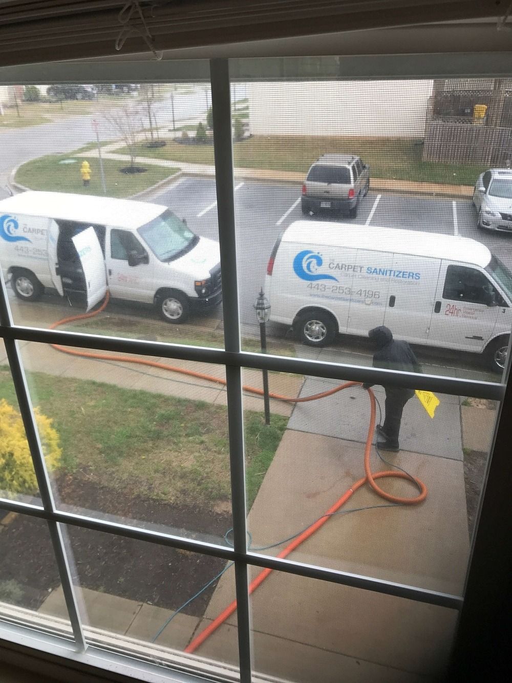 Two white vans parked outside, one with an open door. A person is spraying a sidewalk with a hose.