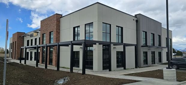 Modern two-story building with brick and light grey facade. Black-framed windows and a dark pergola. Cloudy sky.