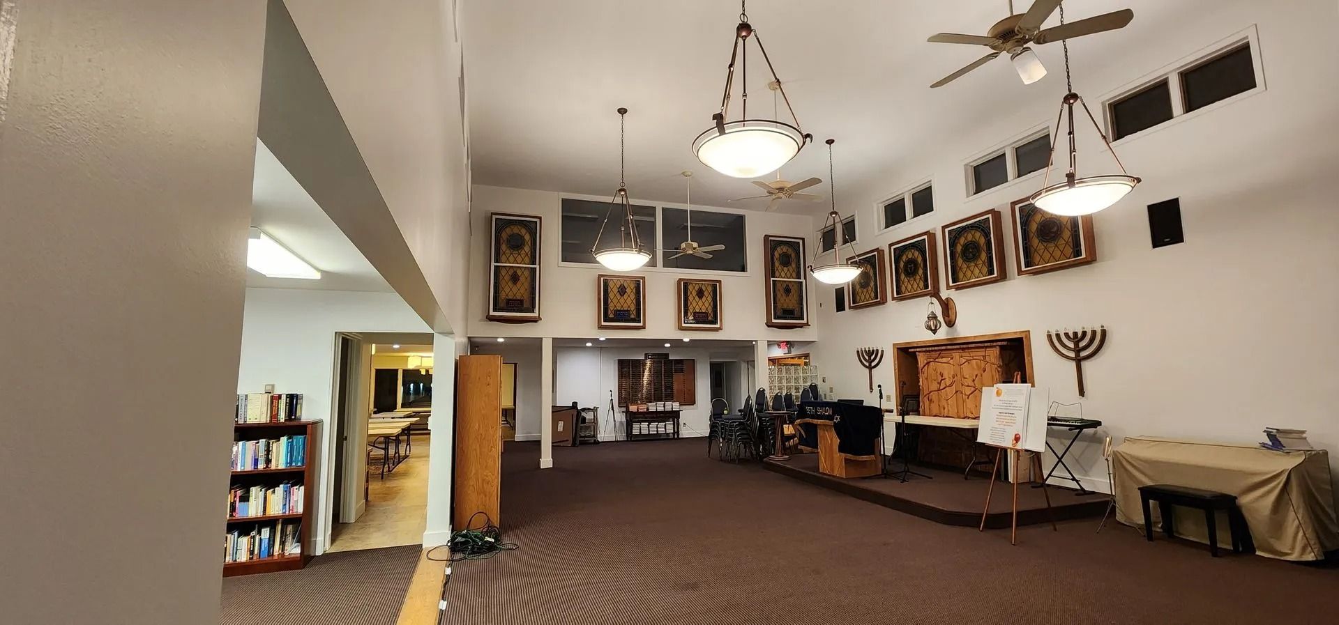 Interior of a synagogue with religious items, including a menorah, paintings, and podium.